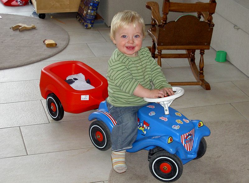 Oskar Vogel auf einem blauen Spielzeugauto mit rotem Anhnger. Fotograf unbekannt